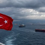 Ön planda Türk bayrağı ve fırtınalı bulutların altında Karadeniz’de seyreden ticari gemiler