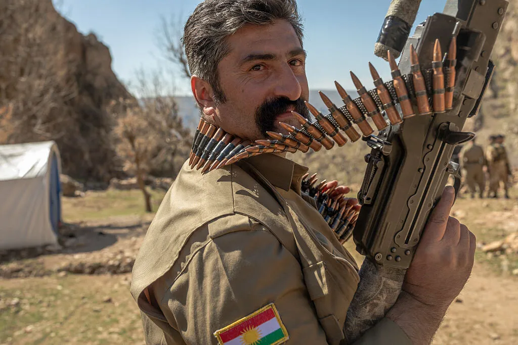 Irak Kürdistan Bölgesi’nde dağlık bir alanda, üniformasında Kürdistan Bölgesi bayrağı bulunan silahlı bir Kürt gücünün görüntüsü. Görsel, Irak’ın Kürt bölgelerindeki silahlı güçlerin varlığını ve son gerilimlerle birlikte bölgede öne çıkan güvenlik ortamını yansıtıyor.