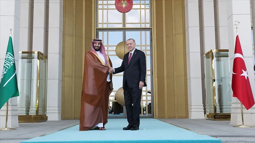 Türkiye Cumhurbaşkanı Recep Tayyip Erdoğan, iki ülkenin bayrakları önünde Suudi Arabistan Veliaht Prensi Muhammed bin Selman ile tokalaşırken; görüntü Ankara ile Riyad arasında gelişen siyasi ve savunma iş birliğini yansıtıyor.
