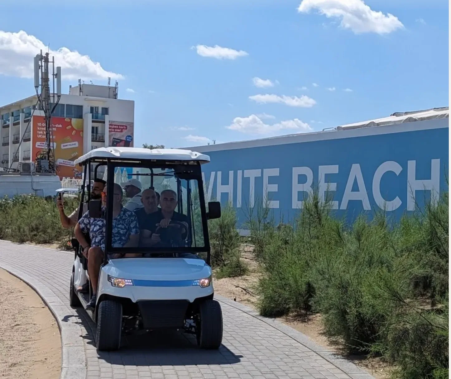 Bakü’deki Sea Breeze sahil kompleksini ziyaret eden bir grup misafir; ziyaretçiler elektrikli araçla tesis alanını gezerken arka planda büyük “WHITE BEACH” tabelası görülüyor.