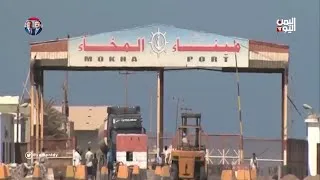 Yemen’deki Muha Limanı’nın “Mokha Port” yazılı giriş kapısı; giriş alanında insanlar, yük araçları ve liman ekipmanları görülüyor.
