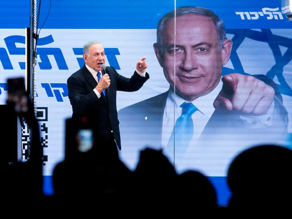 Binyamin Netanyahu, büyük portresinin ve Likud logosunun önünde düzenlenen seçim mitinginde kalabalığa hitap ederek eliyle işaret ediyor.