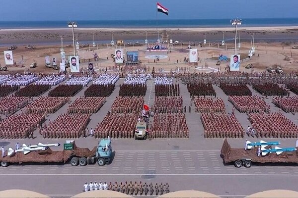 Yemen’deki askerî geçit töreninin havadan görünümü; kıyıya yakın alanda düzenli birlik safları, Yemen bayrağı ve insansız hava araçları taşıyan kamyonlar görülüyor.